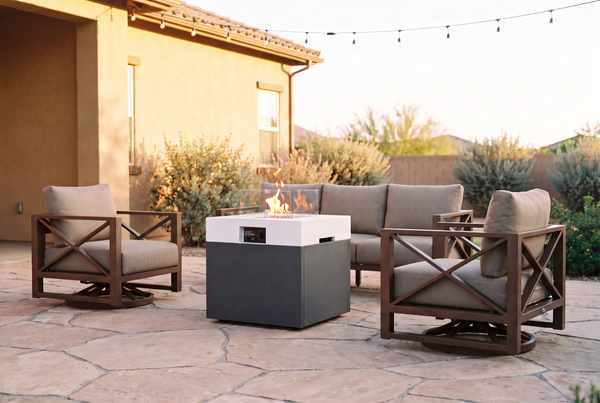Fire pit table with lit flame and glass wind guard surrounded by aluminum patio chairs at dusk, styled for a fire pit set buying guide