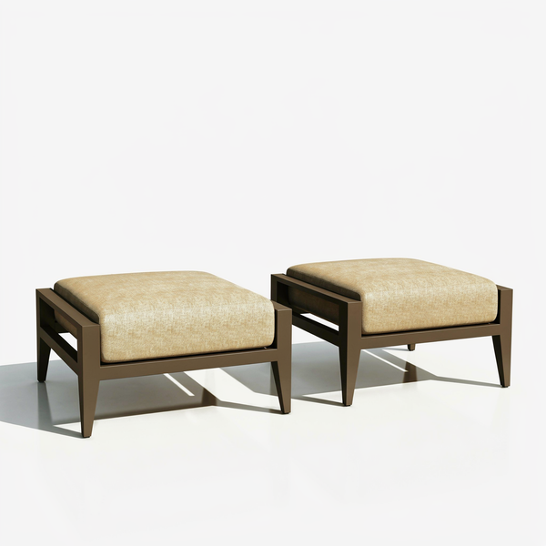 Two Maison Backyards aluminum patio ottomans with thick beige cushions and bronze frames on studio background