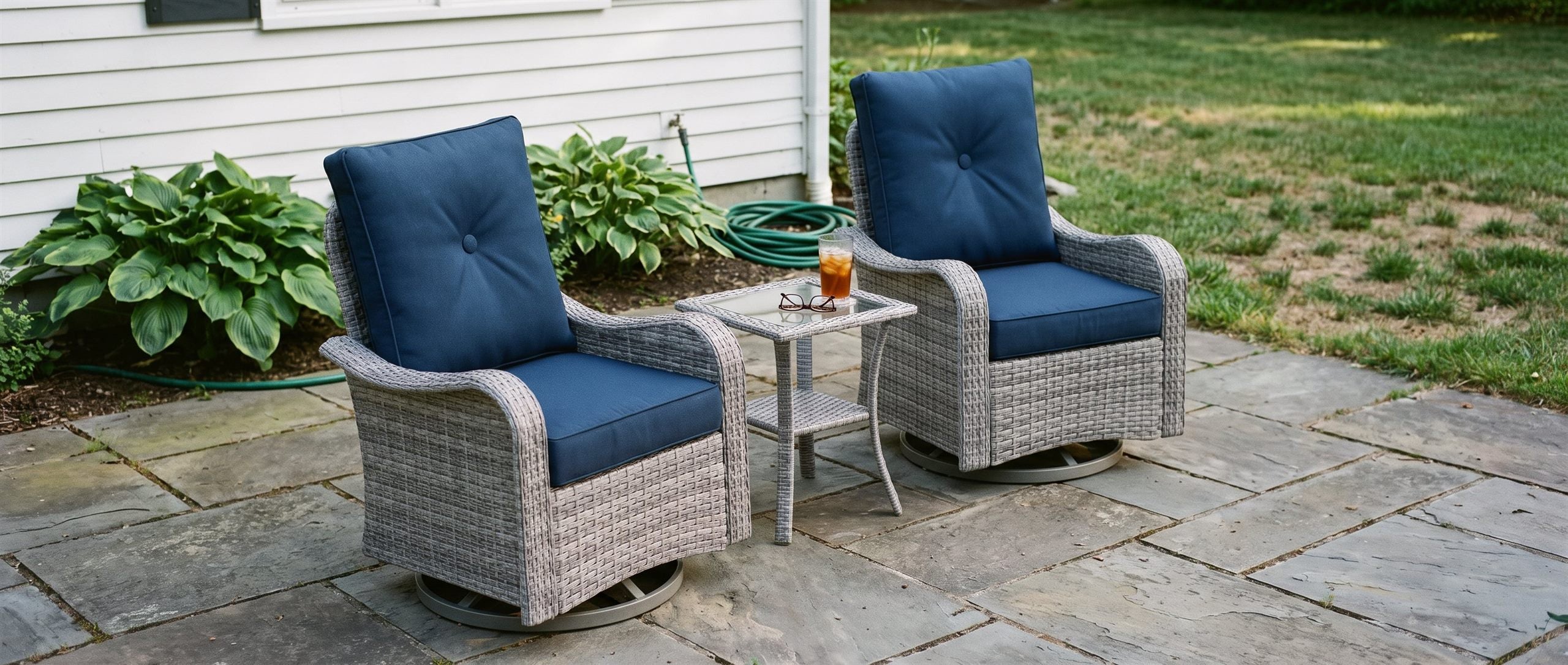 Grey wicker swivel rocking chairs with navy cushions on a shaded stone patio