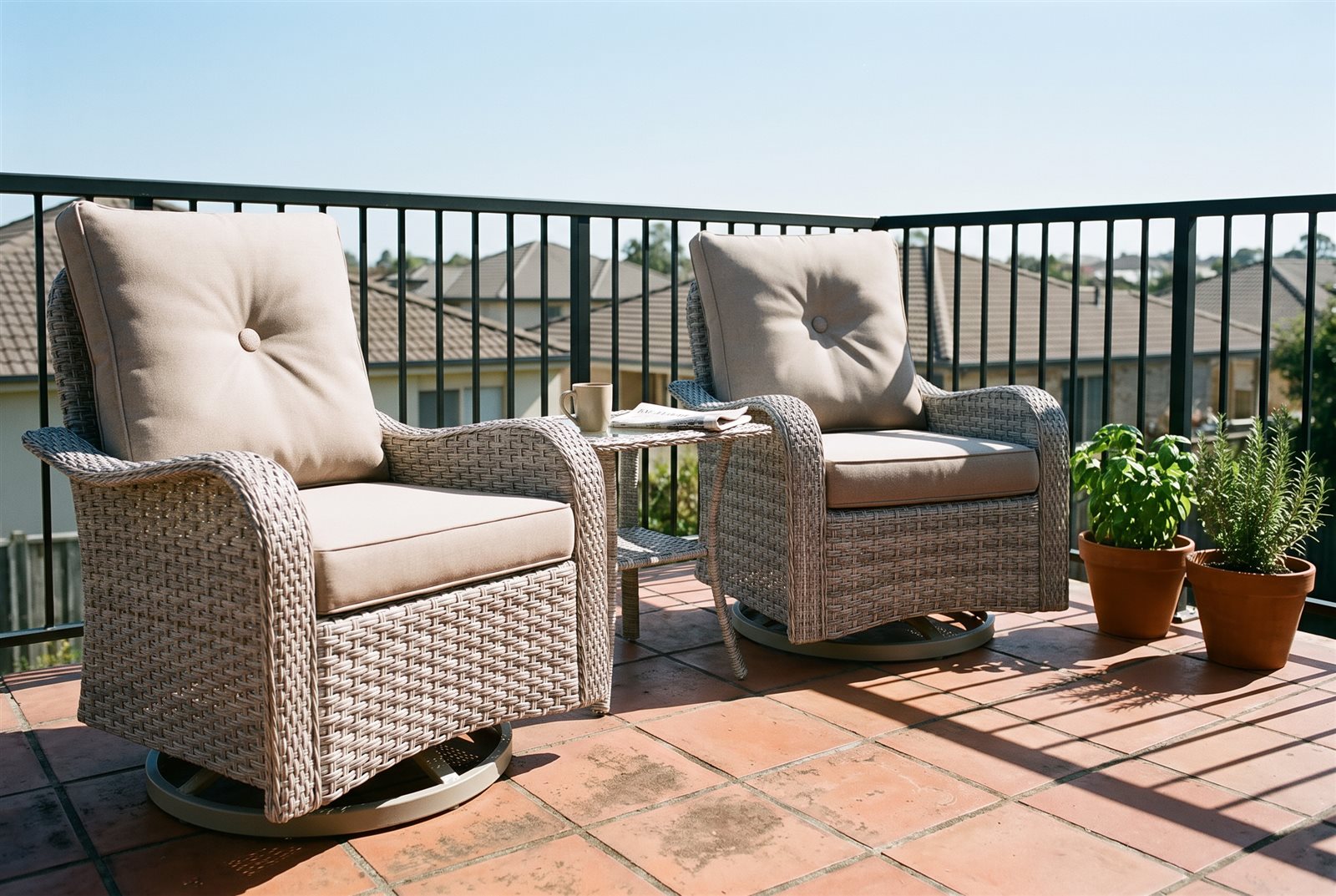 Two wicker swivel rockers with a side table on a small tiled balcony in morning sun